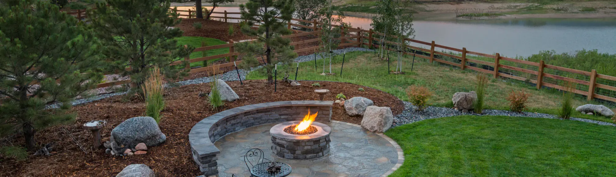 Residential patio with fire pit, curved stone bench, and lake view at sunset.