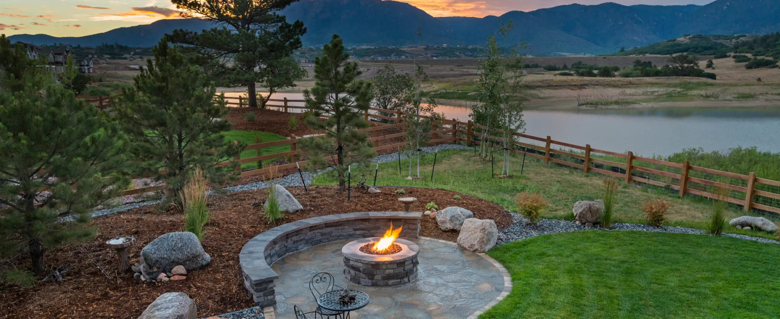 Residential patio with fire pit, curved stone bench, and lake view at sunset.