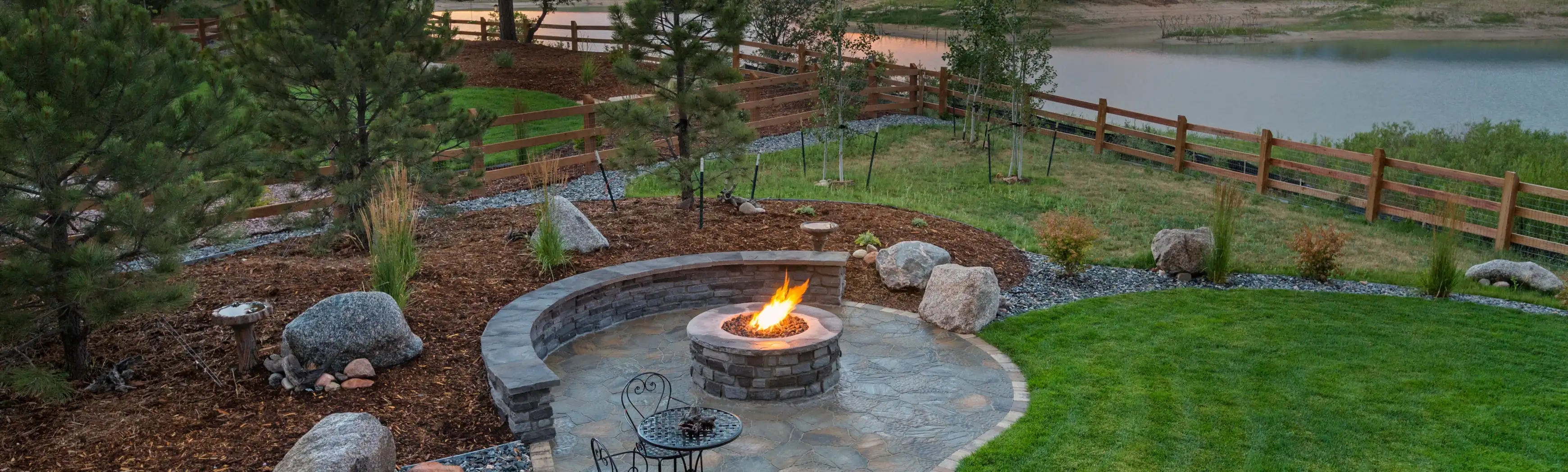 Residential patio with fire pit, curved stone bench, and lake view at sunset.