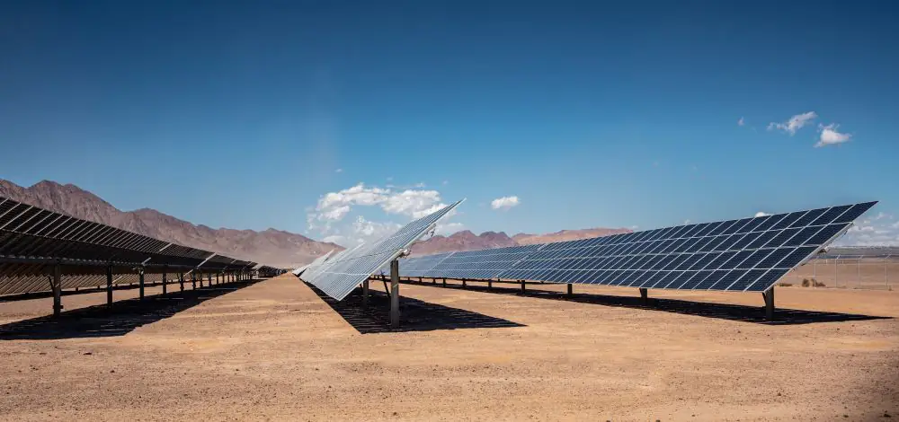 Solar farm in desert terrain with rows of angled solar panels under clear blue sky.