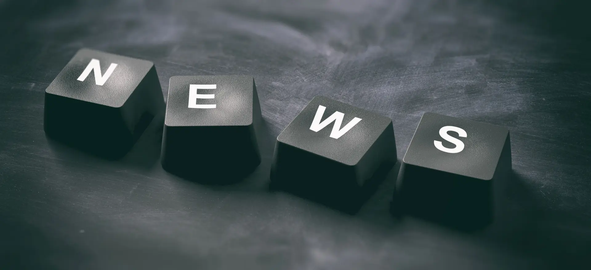 Black keyboard keys spelling “NEWS” on a dark surface, representing digital updates and public communication.