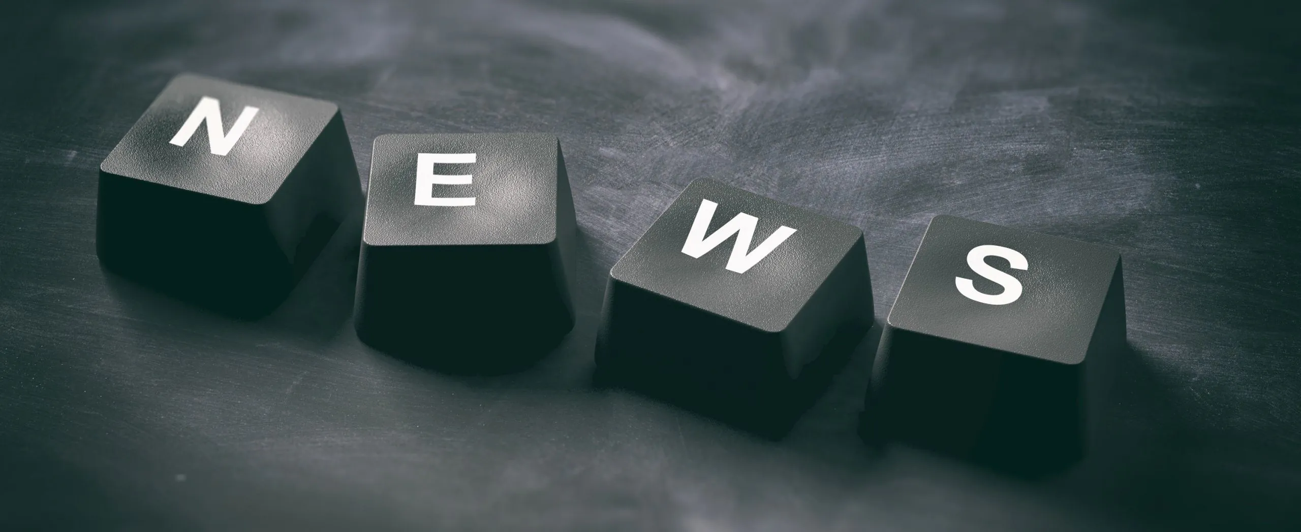 Black keyboard keys spelling “NEWS” on a dark surface, representing digital updates and public communication.