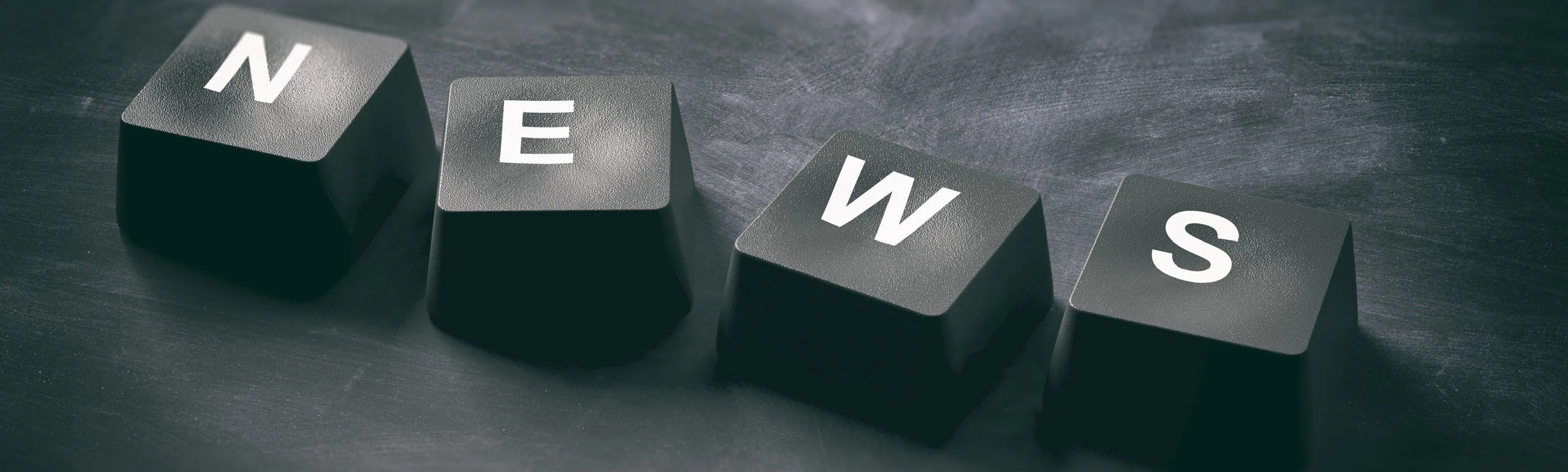 Black keyboard keys spelling “NEWS” on a dark surface, representing digital updates and public communication.