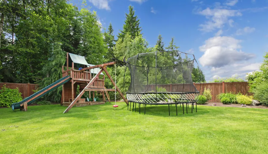 Residential backyard with play structure, trampoline, and surrounding greenery.