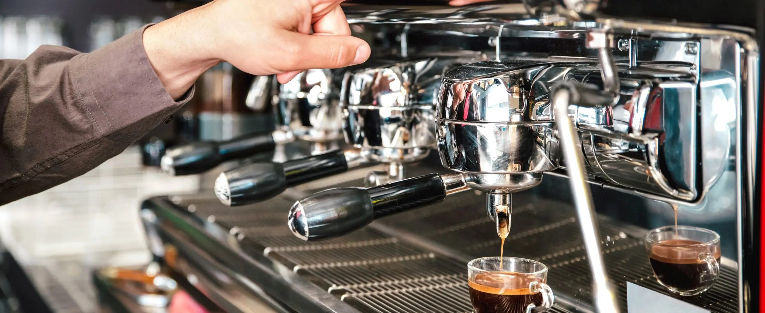 Commercial espresso machine dispensing coffee into glass cup in professional setting.