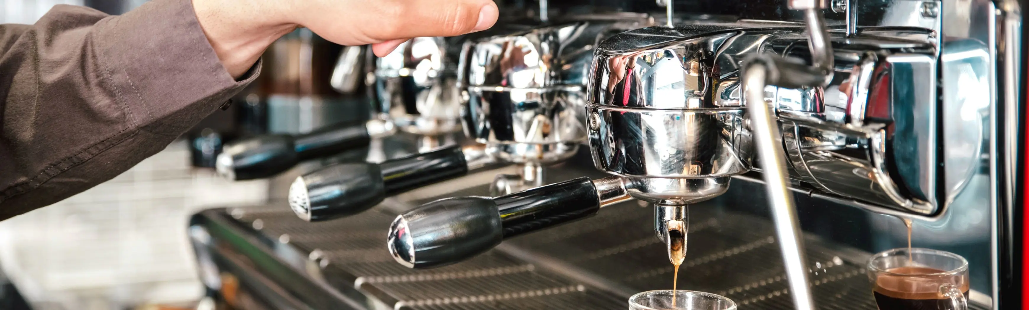 Commercial espresso machine dispensing coffee into glass cup in professional setting.
